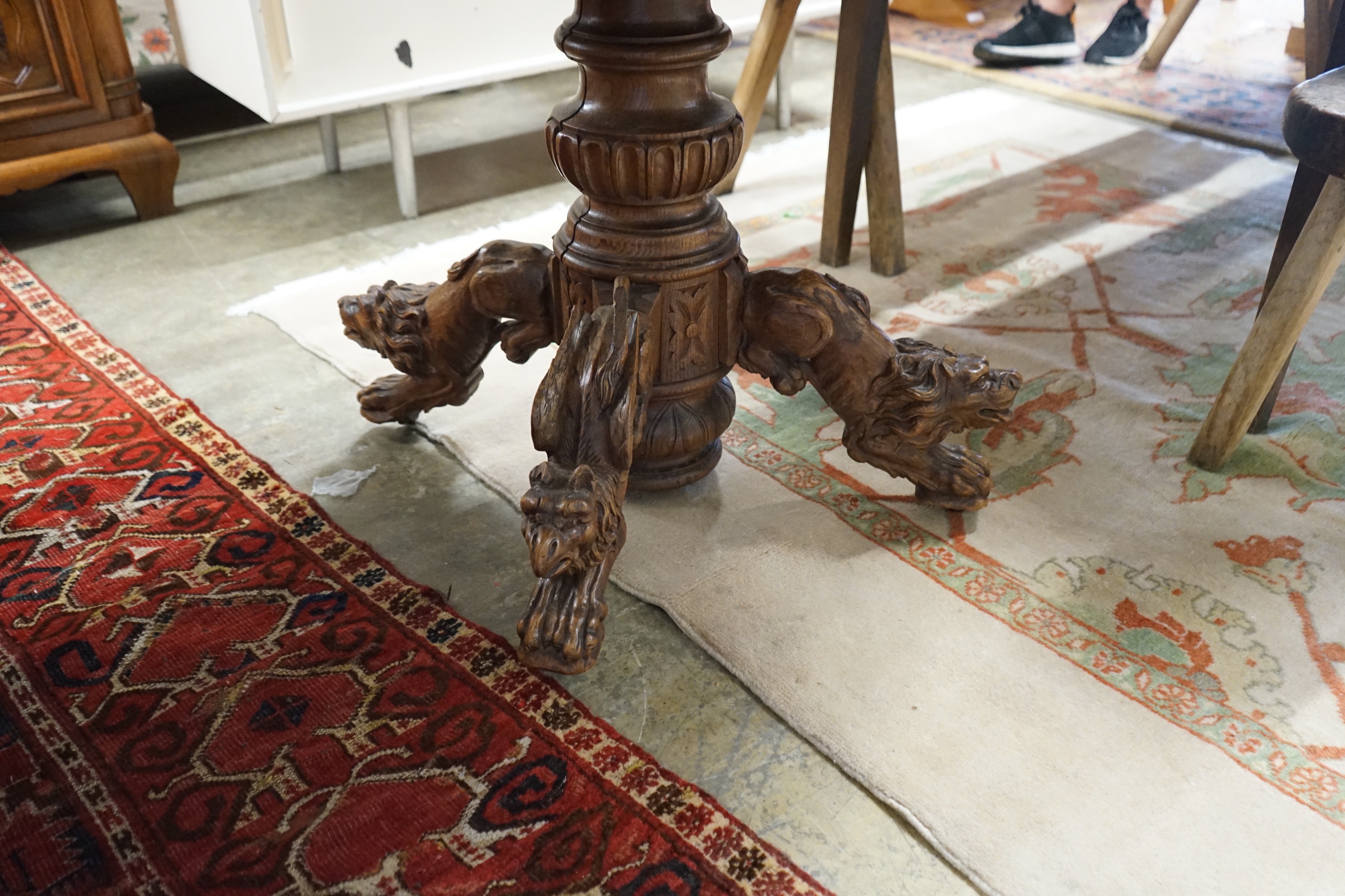 An early 20th century Continental carved oak circular centre table with heraldic tapestry top on winged lion supports, diameter 102cm, height 74cm